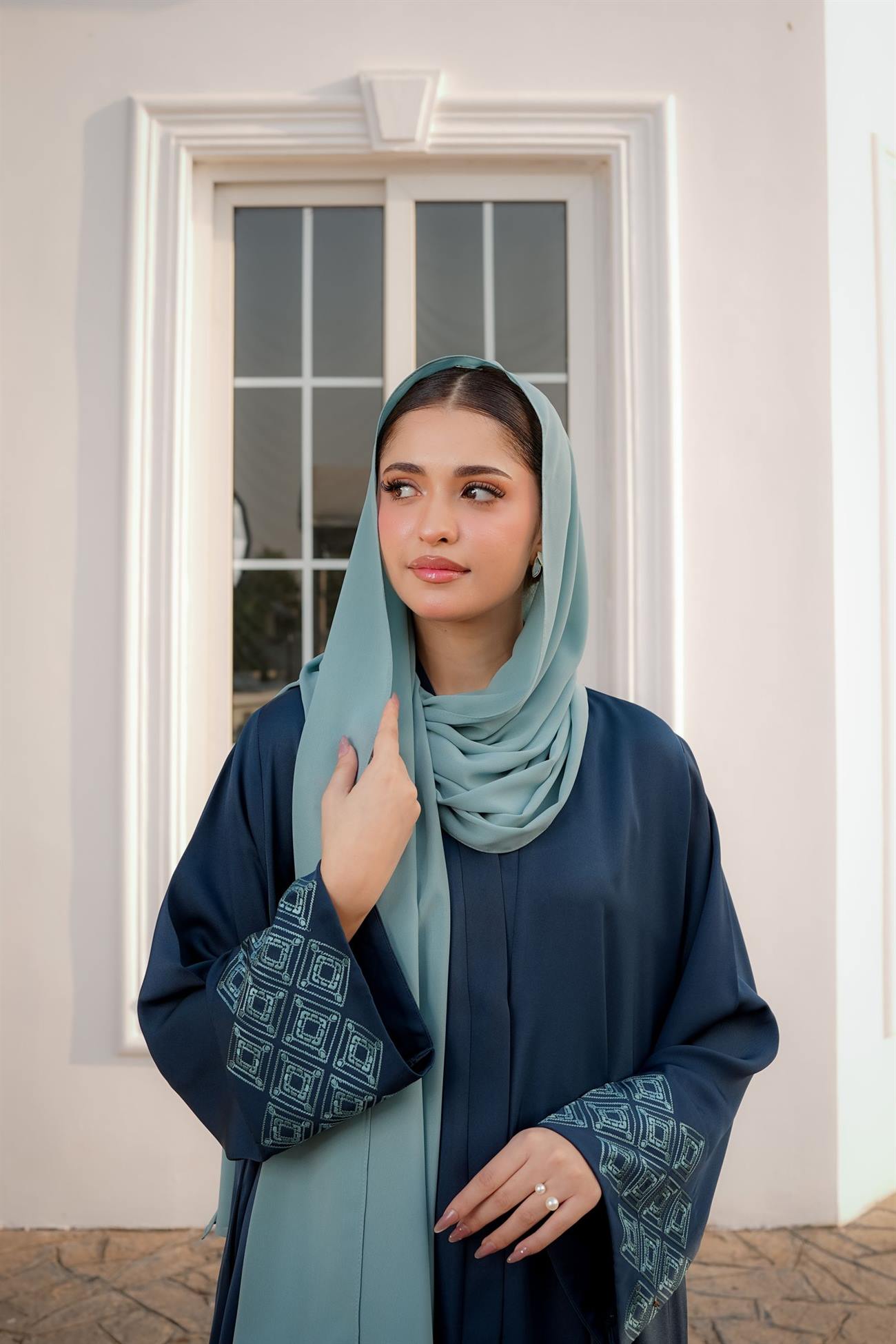Model in a deep teal abaya with patterned cuffs