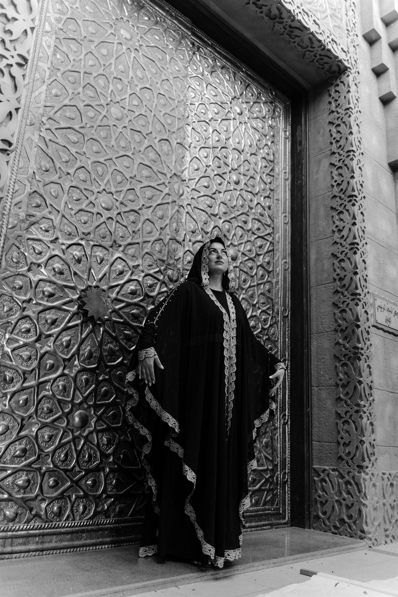 Model in an embroidered black abaya by an ornate doorway